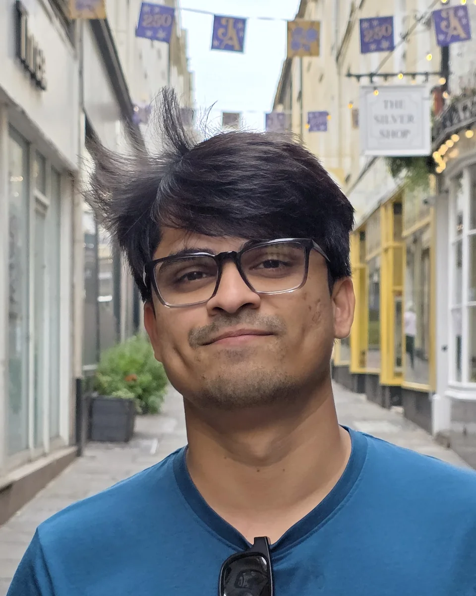Pranav Kushwaha in glasses and a blue T-shirt, smiling in a narrow shopping lane